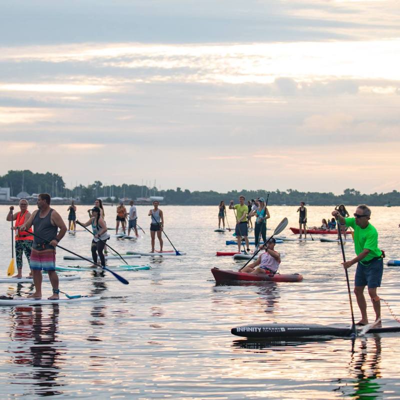 People paddleboarding and kayaking on calm water during sunset.