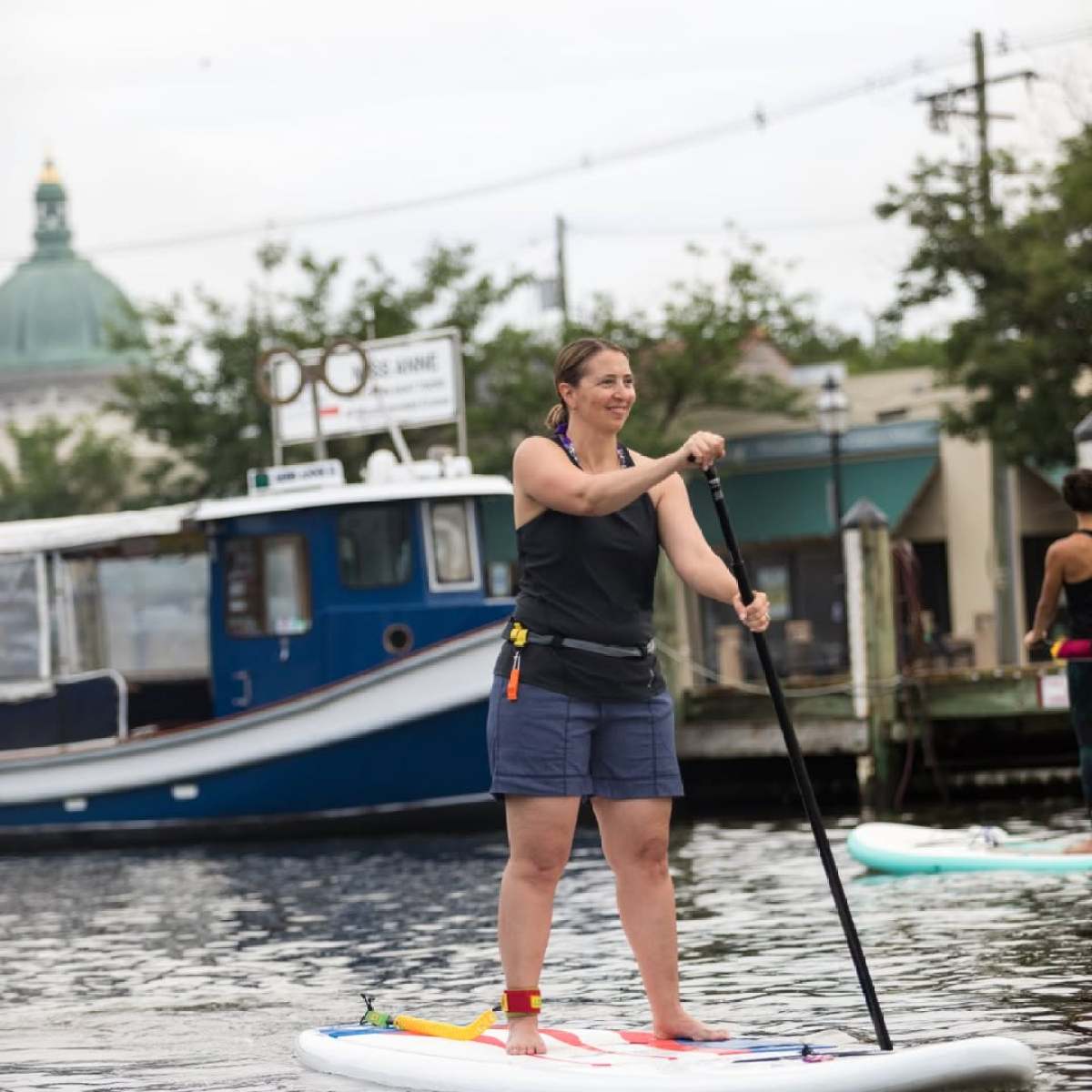 Person paddleboarding on calm water near docked boat.