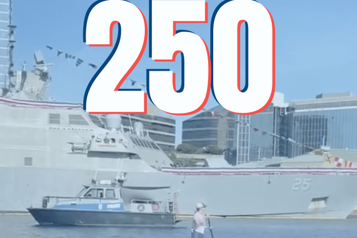 Paddleboarder on water near large ship with 'SAIL 250' text overlay.