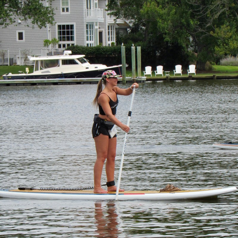 Woman paddleboarding on a river near a house and boat dock.