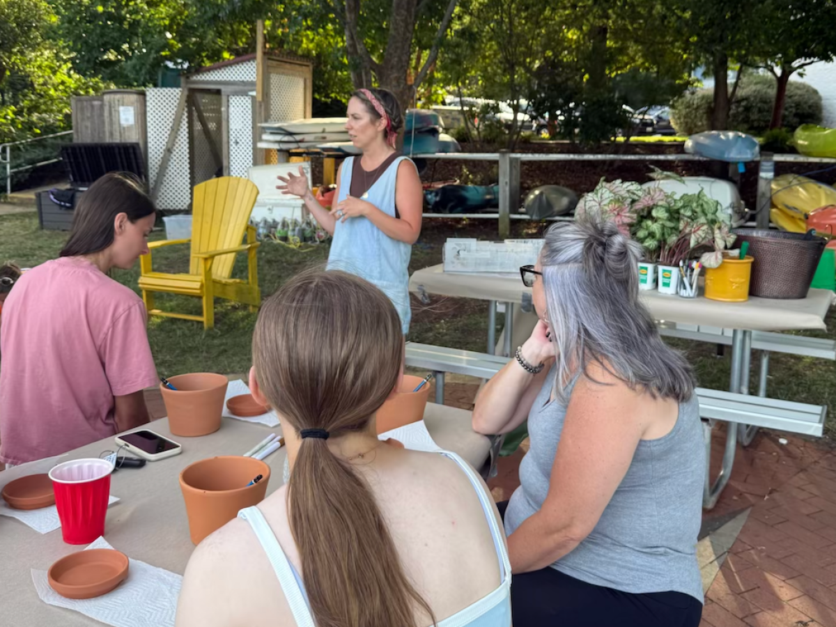 Outdoor flower arranging class with instructor and participants seated at a table.